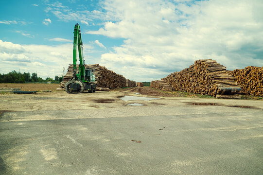 S&auml;gewerk - Holzverarbeitung - Wood Storage - Old green log handling machine and a huge pile of logs in a rural area in cloudy sky background