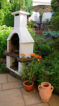 Grillkamin / Steingrill an einer Gartenterrasse mit Blick auf eine weitere Sitzecke mit Sonnenschirm und diversen Pflanzen
