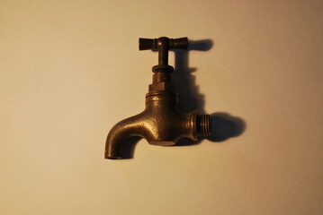 antique object - faucet - made of brass on a light background, under warm artificial lighting - obrazy, fototapety, plakaty