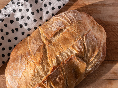 Angled close up view of a loaf of sourdough bread on a rustic wooden cutting board and tea towel