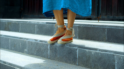 Fototapeta na wymiar Legs of a European girl in a blue dress walking in shoes along a stone