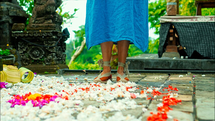 Legs of a European girl in a blue dress walking in shoes along the road with antique stonework along a green park with flowers