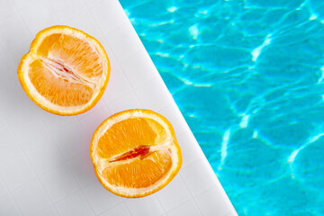 Aerial view halves of orange on poolside with cool blue pool water waves.