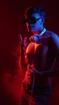 Seductive man. Sexy dancer. Nightclub party. Hot handsome confident flirting topless six pack torso guy dancing in bright colorful neon light at night vertical.