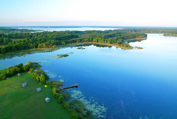 Lake in wild nature, aerial view. Lake on sunset in summer. Aerial panoramic landscape view of lake in wildlife. Drone view of wetland in green colors. Rural environment, clean air and ecology. Pond.