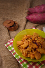 Green plate on burlap with stewed sweet potatoes or yam. Tasty dish, healthy country food. Pepper peas spice pot, raw potatoes on background