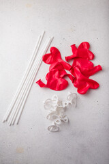 Heap of red heart-shaped not inflated new balloons with sticks holders on white background, top view. Valentines day, wedding, birthday decor