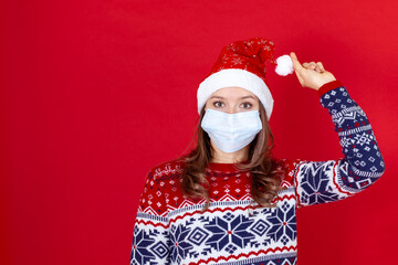 Fototapeta na wymiar close up a young woman in a medical mask, Santa Claus hat holding a pompom on a red background.