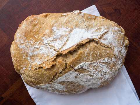 Top view of a loaf of sourdough bread on dark wooden board and white napkin