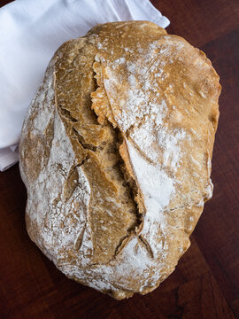 Angled view of a loaf of bread on a dark wooden board and napkin