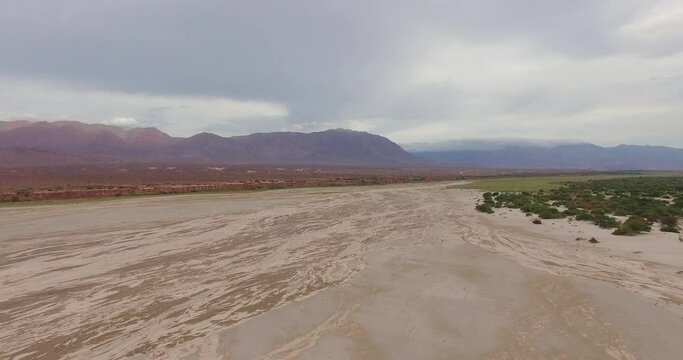 Aerial view of the arid desert, sand, mountains and flora, under a cloudy sky at sunset. 