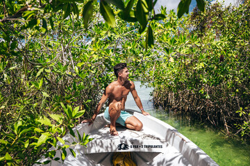 young male tourist on a boat through mangrove river in Tulum Mexico on a sunny summer day - obrazy, fototapety, plakaty