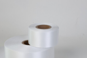 macro side view tower of two coils of white satin ribbons of different sizes for labels or branding, isolated on a white, gray background.