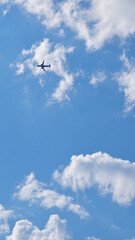 The passenger airplane is flying far away in the blue sky and white clouds. Aircraft in the air. Light vertical background or illustration about international passenger air transportation