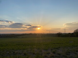 Naklejka na ściany i meble Sunset over the field in England, red sunset behind the cloud in spring time, romantic view