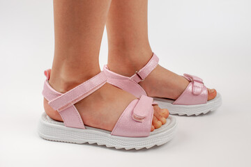 Pink children's sandals made of shiny leather with Velcro fasteners, flat white soles, isolated on...