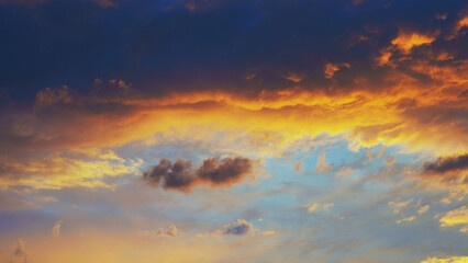 Cloudy sky at sunset. Dark blue and yellow natural background or wallpaper. The rays of the setting sun effectively illuminate the clouds. Beautiful colorful evening skies. Twilight cloudscape