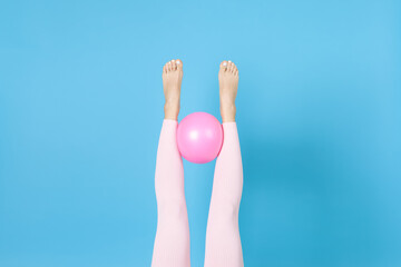 mock up women's legs in pink sports leggings hold a rubber Pilates ball between them, isolated on a blue background.
