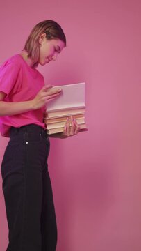 Back to school. Book knowledge. Student lifestyle. Puzzled woman librarian opening pile of homework textbooks isolated on pacific pink background vertical.