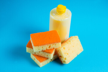 Dishwashing liquid in a transparent plastic bottle and porous yellow cleaning sponges on a blue background. The concept of ecological detergents