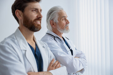 Two doctors with crossing arms in uniform standing in medicine clinic hall and looking away