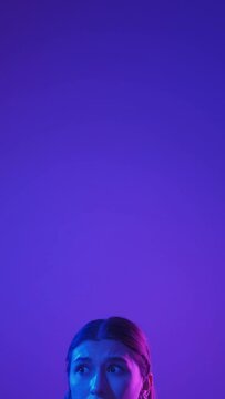 Scared woman. Worried face. Neon light portrait. Uncertain afraid emotion girl in colorful bright glow on purple empty space background vertical.