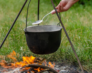 a pot in which soup is cooked on a tripod stands on a fire