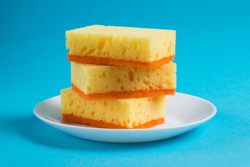 Sponges for washing dishes and cleaning in the apartment on a plate on a blue background. The concept of using ecological detergents for the home