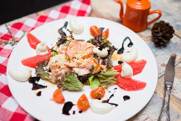 salad with baked salmon (red fish meat), lettuce leaves, cherry tomato slices, grapefruit slices, with cream sauce and ground nuts. the salad is dressed with balsamic sauce.
