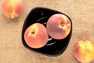Several juicy ripe peaches with a black ceramic plate on a jute cloth, close-up, top view.
