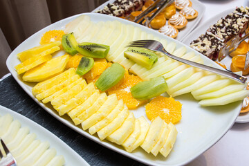 Plate with sliced fruits: pineapple slices, kiwi, orange. Catering serving on a buffet table.