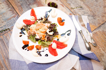 salad with baked salmon (red fish meat), lettuce leaves, cherry tomato slices, grapefruit slices, with cream sauce and ground nuts. the salad is dressed with balsamic sauce.