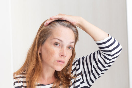 Serious 40s Woman Looking At Gray Hair In Mirror Reflection On Growing Out Root