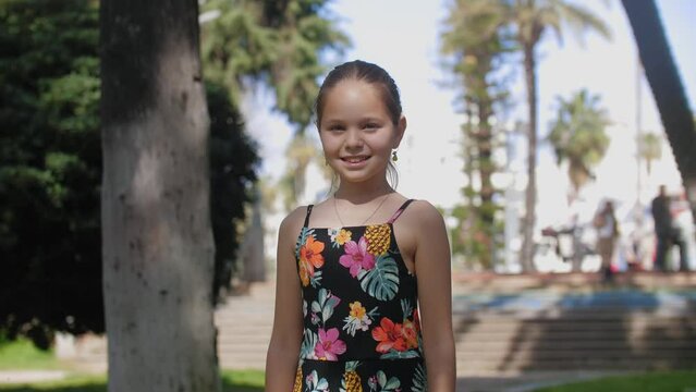 Cute smiling girl stands in the park and looks in the camera