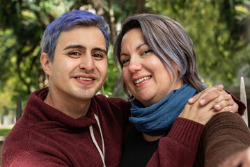 Obraz premium Two smiling friends are hugging and looking at camera. He has blue hair. 