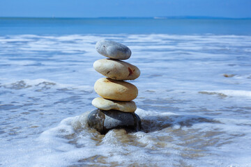 group of stacked stone pebbles on sandy beach with waves incoming. Balance and agility concept. calm beach scene