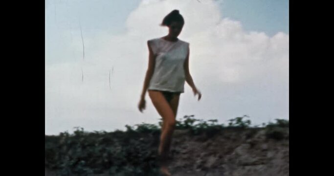 Beautiful model woman in swimsuit in sunny summer, on blue sky, green nature. Girl long, thin legs in Bikini goes in vintage color film. Rest, vacation at weekend. Family archive. Retro 1980s. 4K