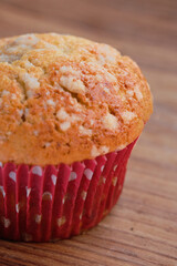 vertical photo of a freshly baked muffin, on a rustic wooden background, with a colorful polka dot wrapper.