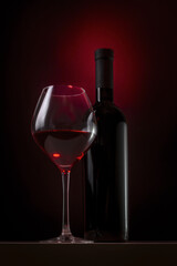 Bottle and glass of red wine on a dark background