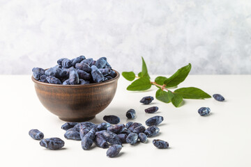Honeyberry (Lonicera caerulea). Sweet honeysuckle berries in a clay bowl on a light background