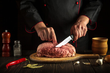 Chef hands with a knife in the kitchen cut raw meat. Cooking delicious food for a restaurant or hotel