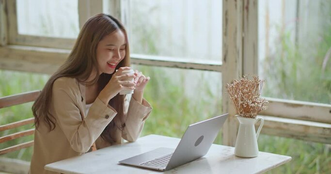 Candid Young beautiful asian woman using laptop surfing on internet during coffee break at cafe. Happy smiling girl looking at computer doing online shopping watching video movie at home. leisure time