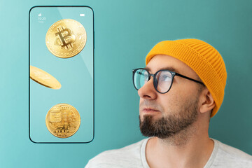 Portrait of a Caucasian young man with glasses and a hat looking at a smartphone showing bitcoins....