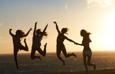 Feeling on top of the world. Silhouette of a group of girlfriends on the beach having lots of fun jumping around.