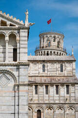 Naklejka premium Leaning tower of Pisa peaking from behind Pisa Cathedral with brilliant blue sky.