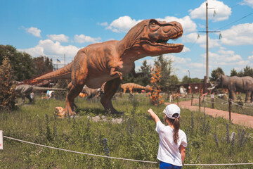 Fototapeta premium A child in a dinosaur park looks at a tyrannosaurus rex.