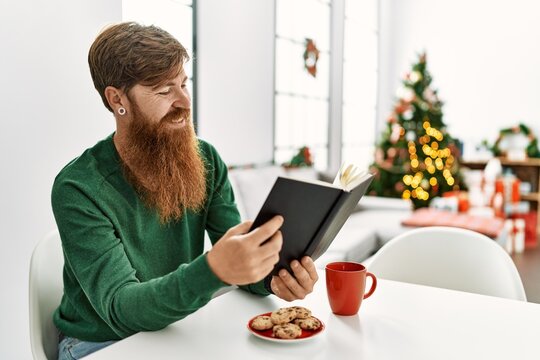 Young redhead man having breakfast sitting by christmas tree at home