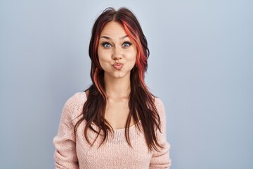 Obraz premium Young caucasian woman wearing pink sweater over isolated background puffing cheeks with funny face. mouth inflated with air, crazy expression.
