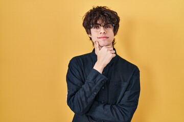 Young man wearing glasses over yellow background looking confident at the camera with smile with...