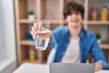 Young hispanic man using laptop drinking water at home